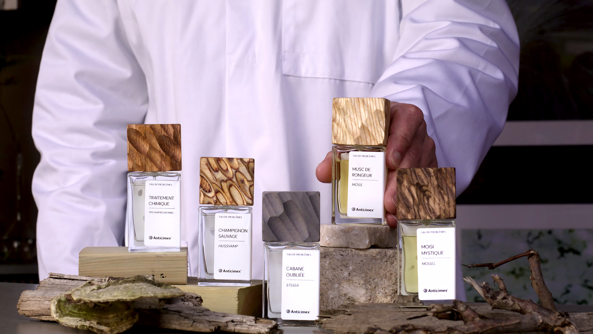 Anticimex Parfymkollektion med fem parfymer uppställda och en man med vit rock som presenterar