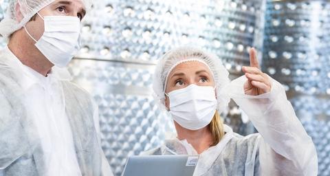 En kvinna och en man i vita skyddsutrustningar står framför behållare av stål