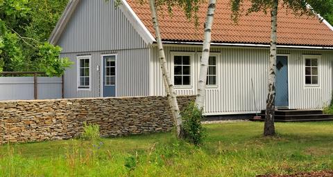 Grått trähus med krypgrund i en grön trädgård