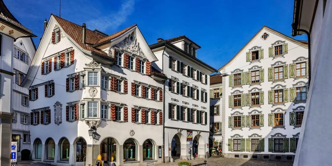 Historic white buildings with red and green shutters on a European street.