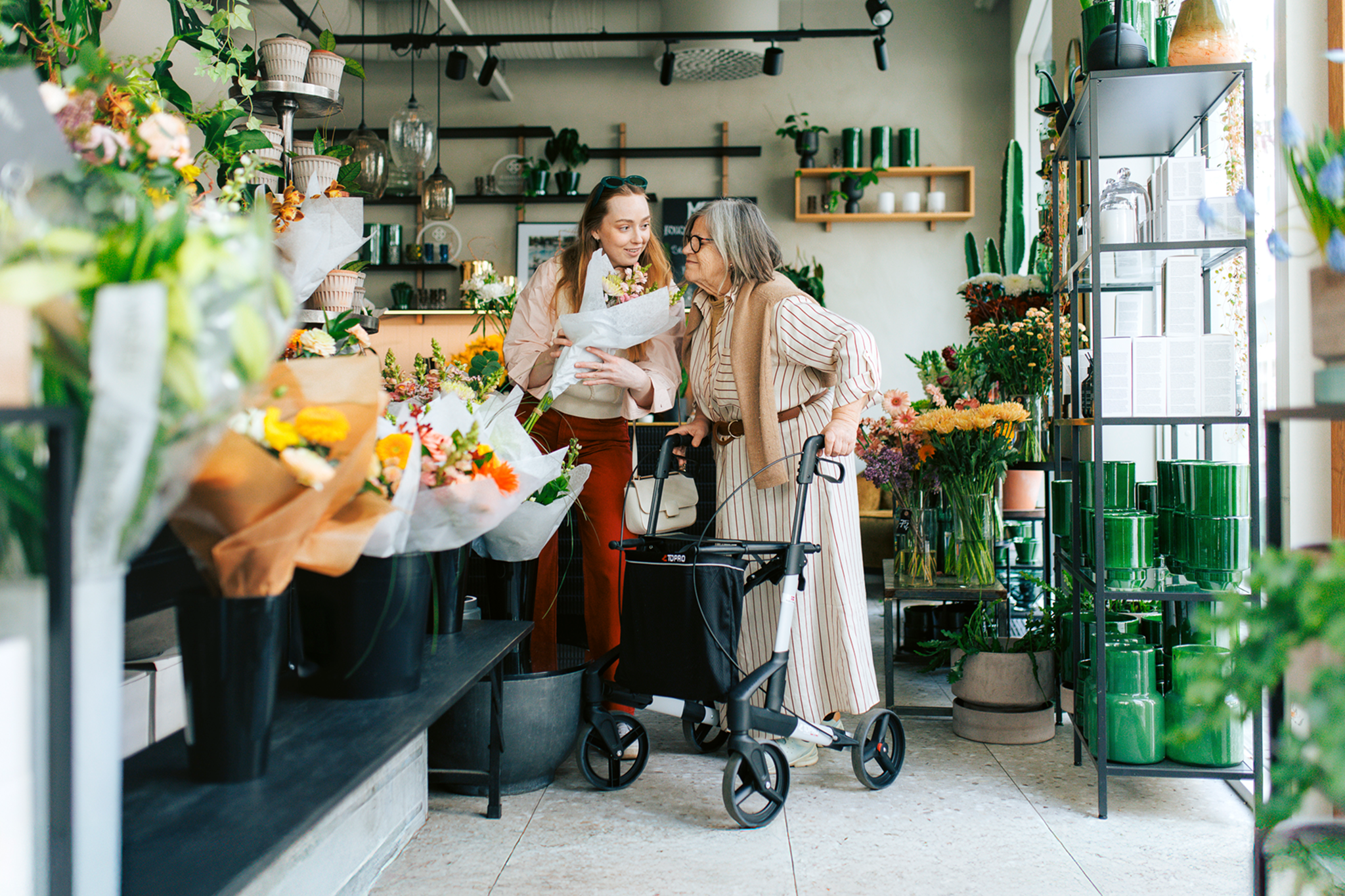 En ung kvinne og en eldre kvinne med rullator handler blomster sammen 