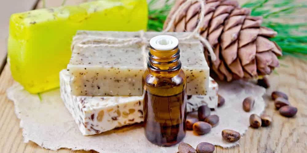 Cedar oil in a bottle, cedar cone, three homemade soap, cedar nuts on the background of wooden boards