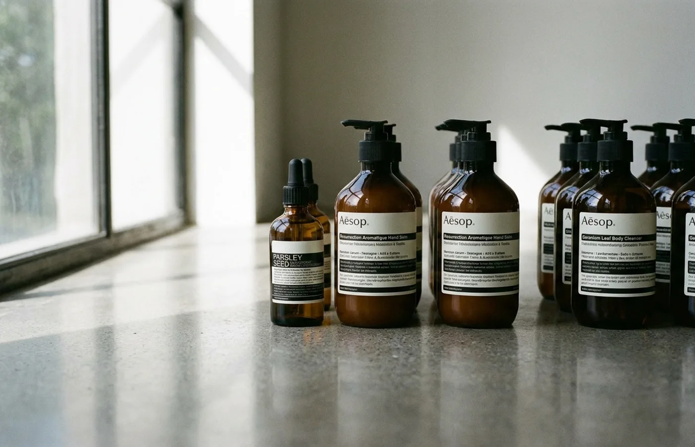 Aesop amber apothecary bottles with minimal black-and-white labels arranged on a marble surface, lit by soft natural side light