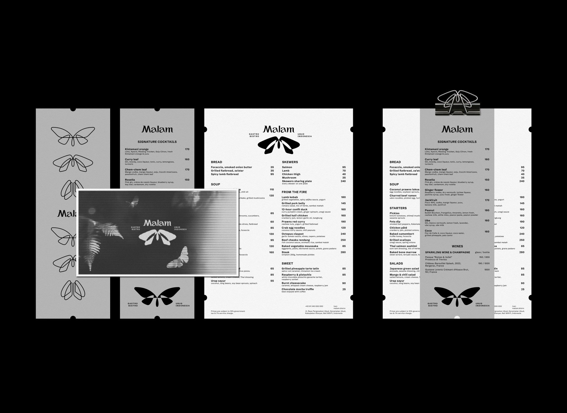 Black-and-white Malam menus and a branded screen arranged on black, with butterfly motifs and a binder clip.