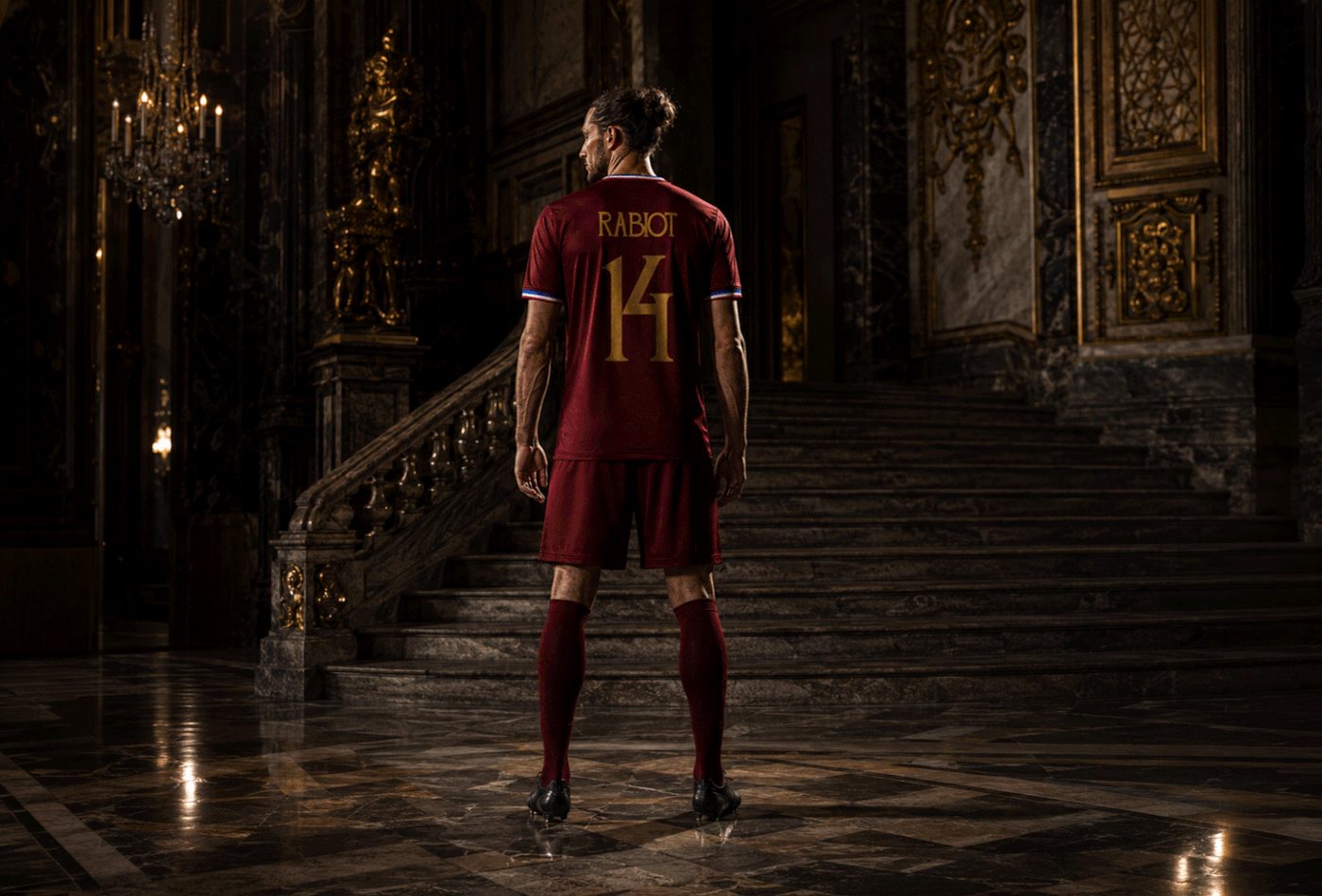 Footballer in a burgundy kit marked “RABIOT 14” in gold stands before a marble staircase in an ornate dark interior.