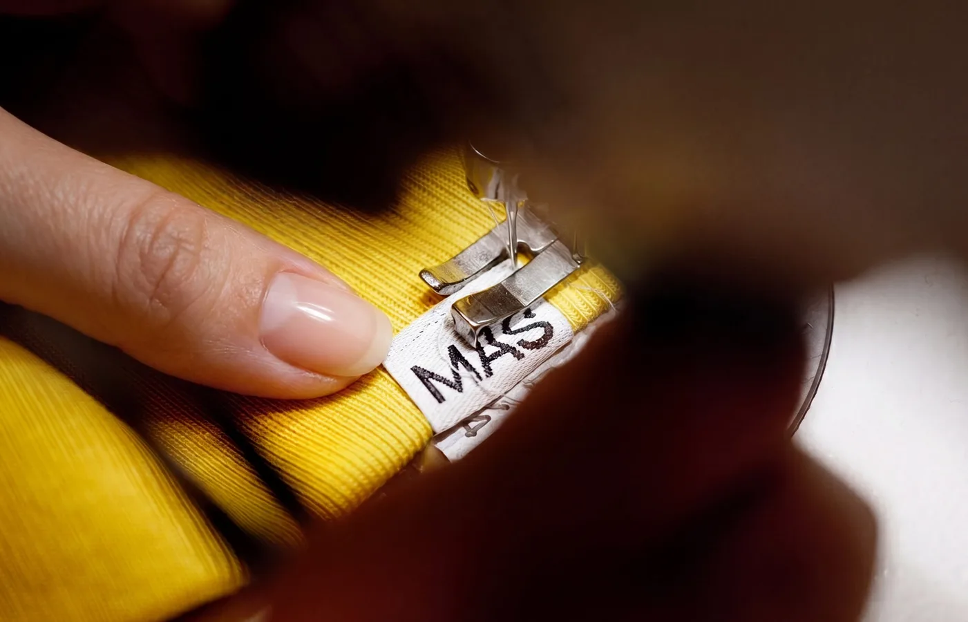 A hand holding a yellow workwear garment with the Mas label stitched into the seam
