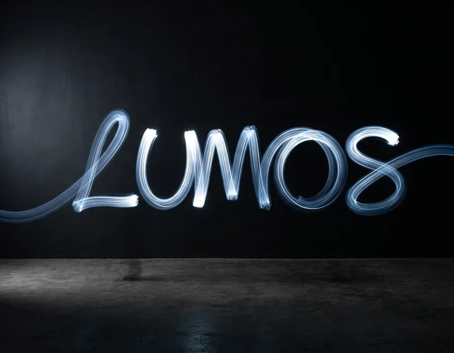 A light-painted brand wordmark captured in long exposure against a matte black backdrop, visible motion trails leaving a gradient arc