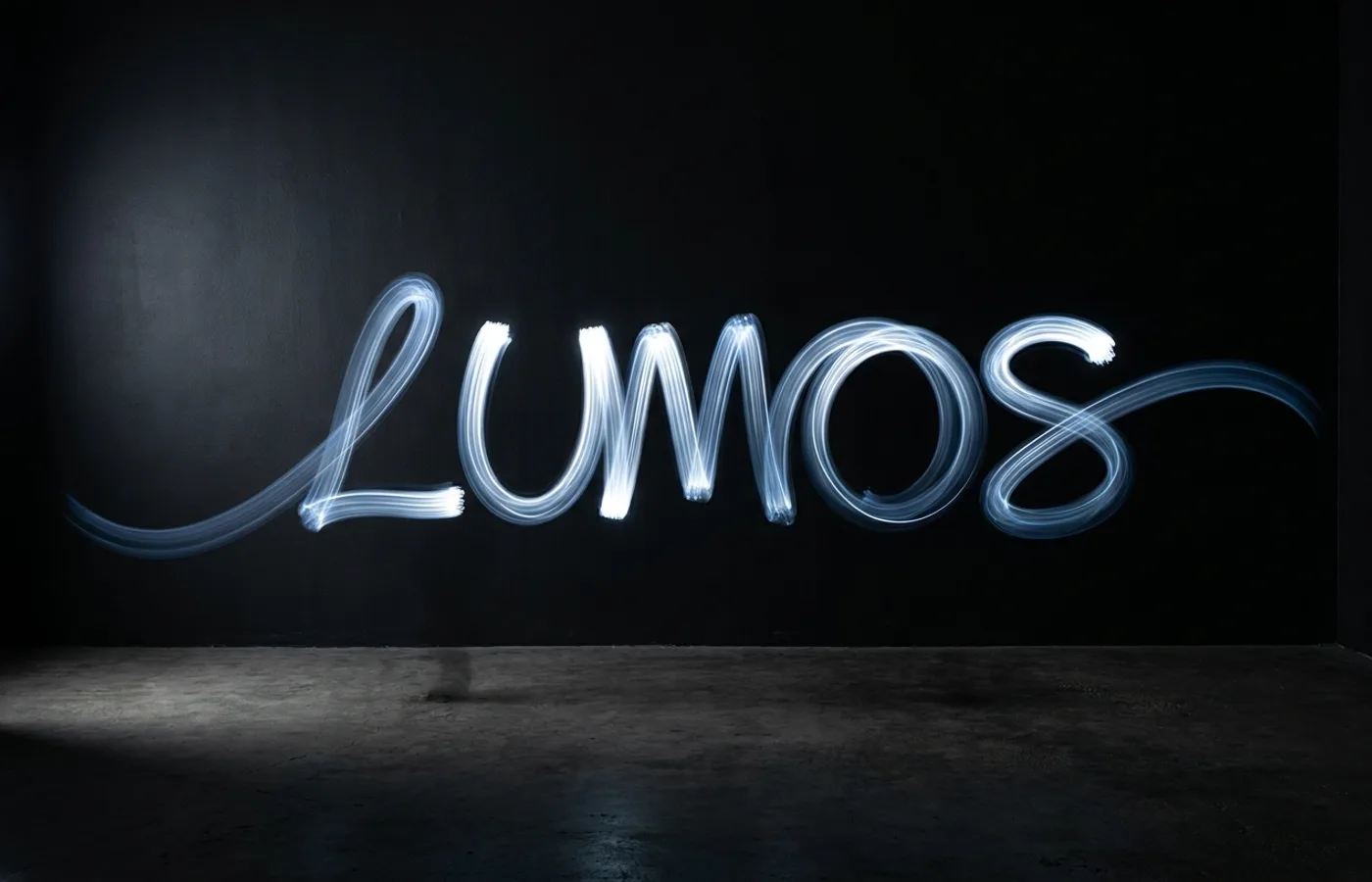A light-painted brand wordmark captured in long exposure against a matte black backdrop, visible motion trails leaving a gradient arc