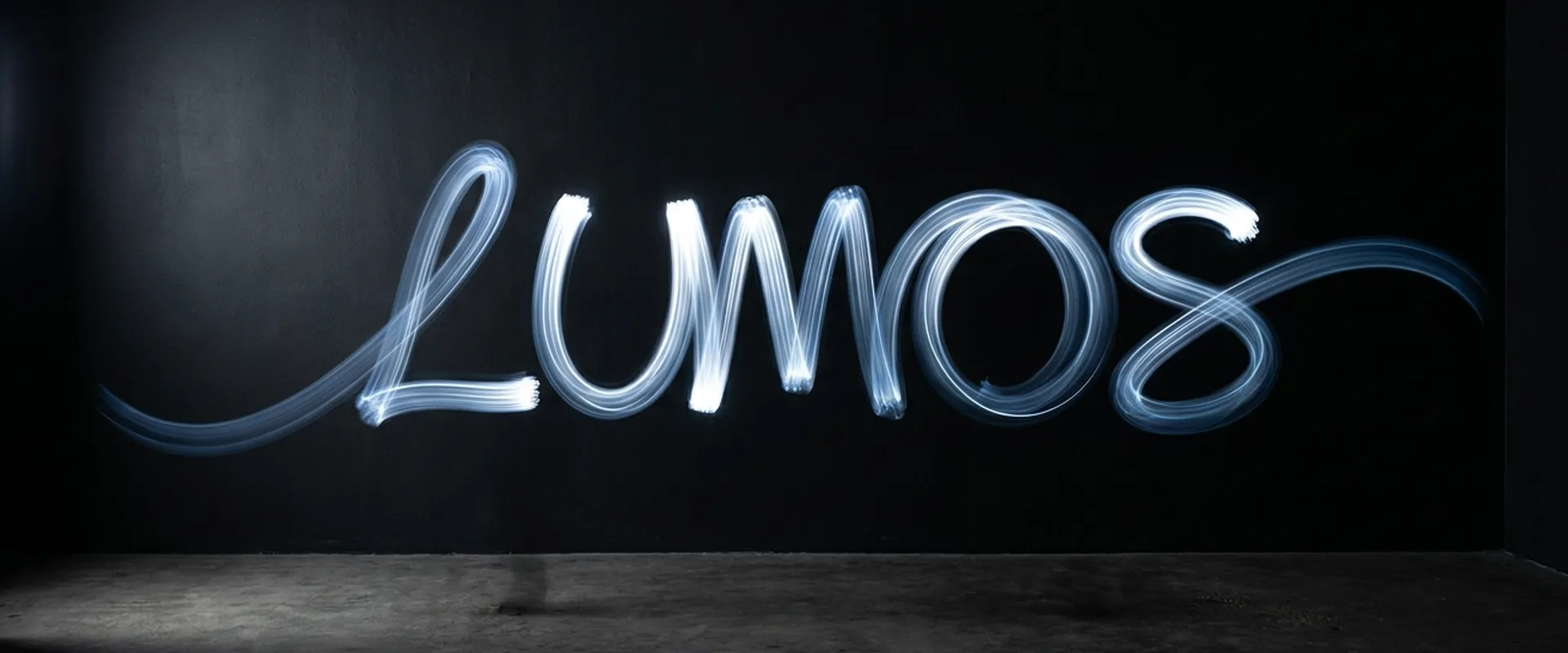 A light-painted brand wordmark captured in long exposure against a matte black backdrop, visible motion trails leaving a gradient arc