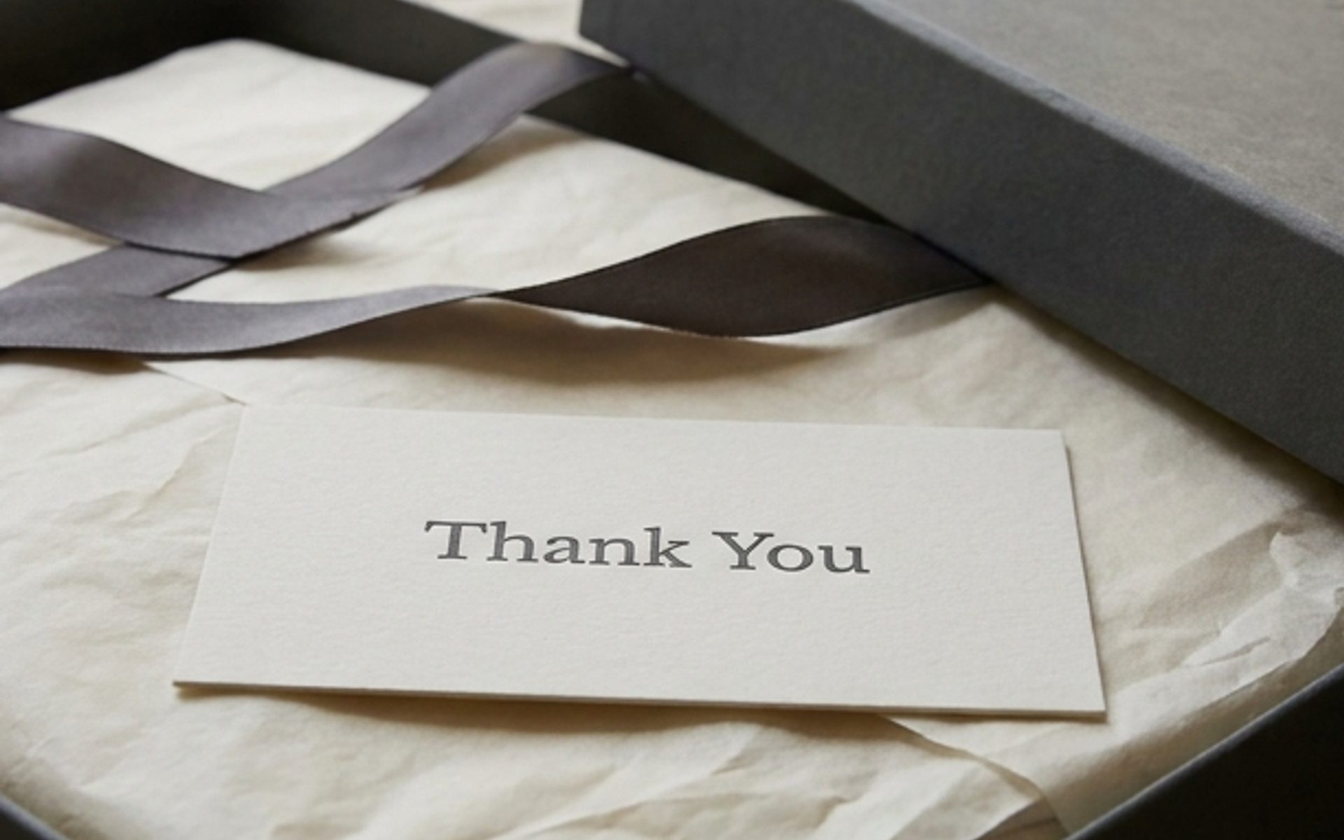 A luxury unboxing moment — a rigid box opened to reveal tissue paper, ribbon, embossed details and a letterpress card on a marble surface