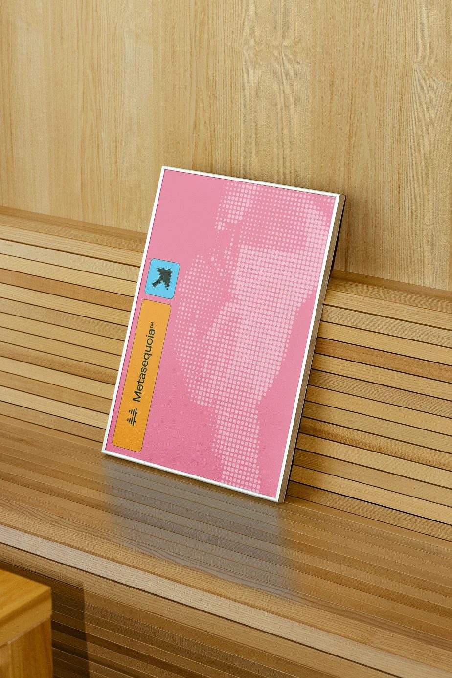 Pink Metasequoia™ poster with a white halftone tree, orange label and blue icon, leaning on a slatted wooden bench.