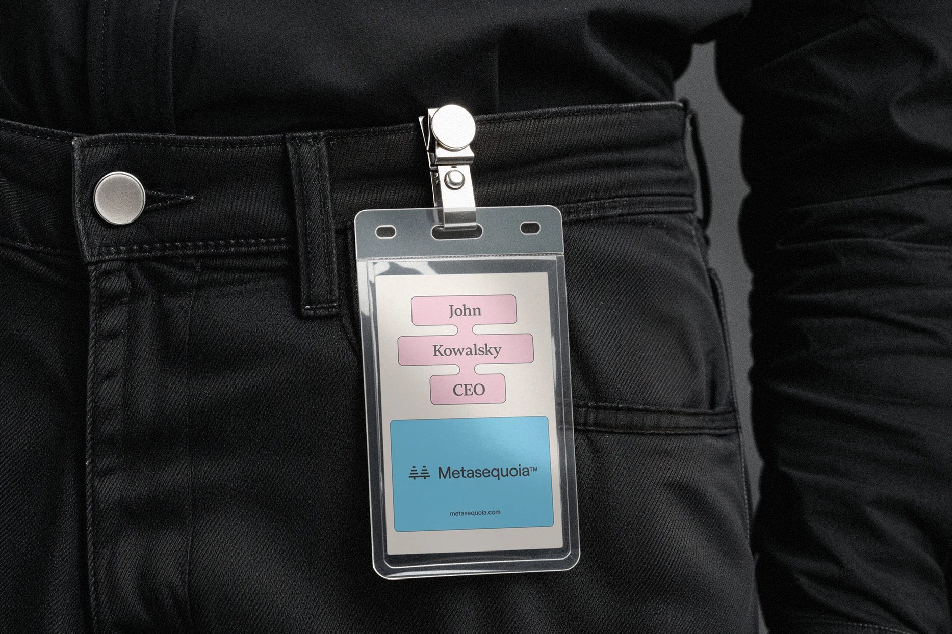 Plastic ID badge clipped to black jeans, with pink labels reading “John Kowalsky CEO” above a blue “Metasequoia™” panel.