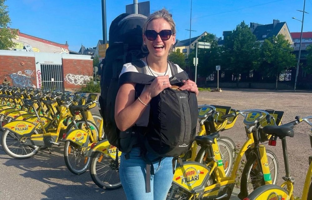 Jen smiling with a large backpack beside a row of yellow rental bikes while travelling solo