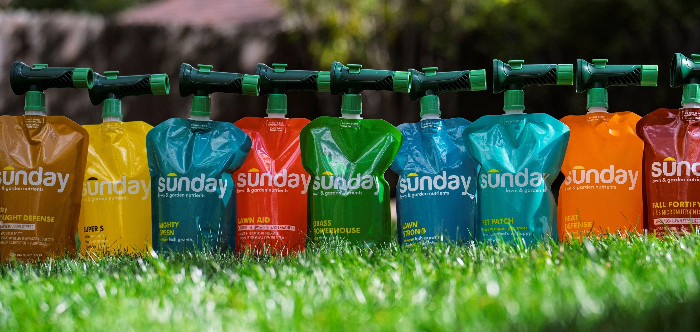 A line of colorful Sunday lawn and garden nutrient pouches with sprayers on green grass.