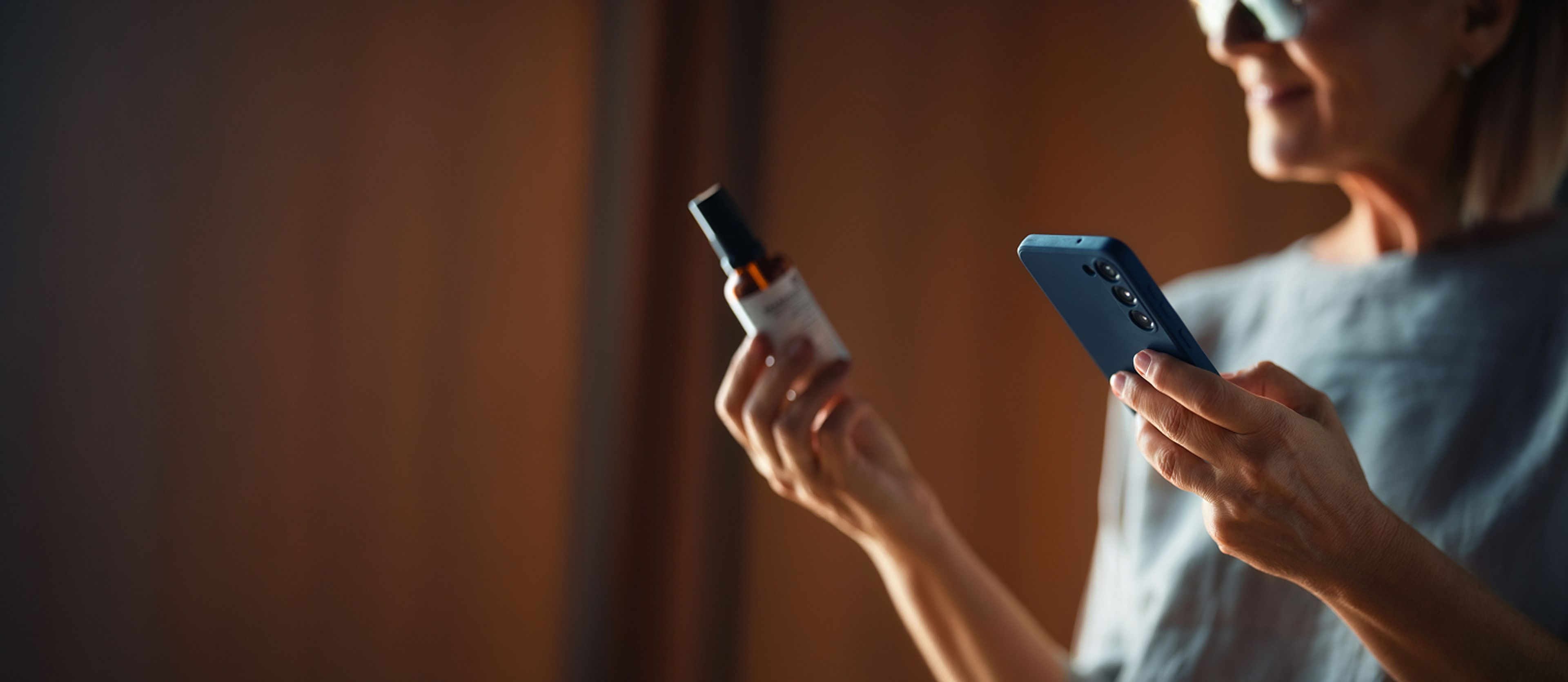 A woman holds a product bottle in one hand and a smartphone in the other, appearing to scan the bottle.