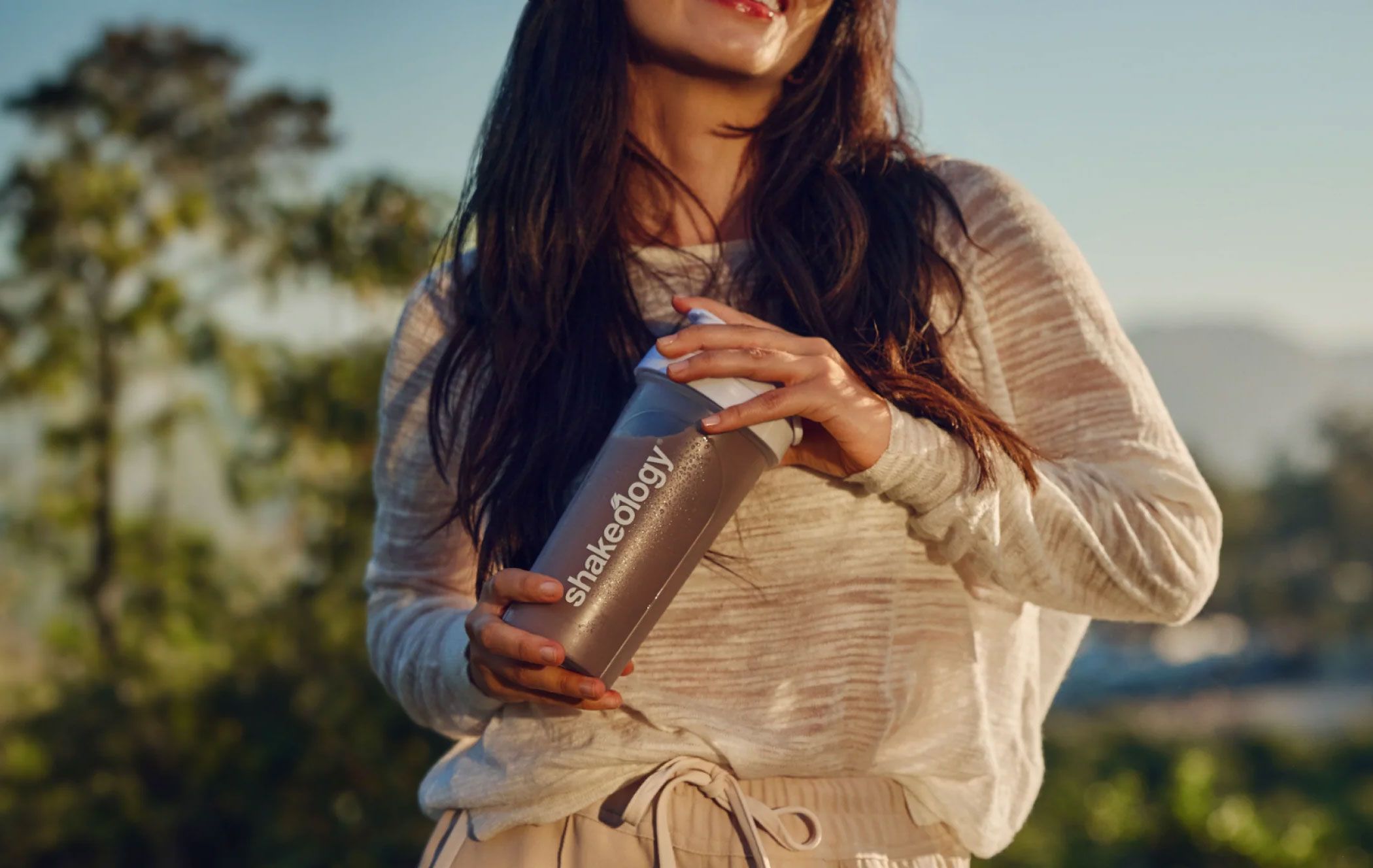 A person holds a Shakeology shaker bottle outdoors.