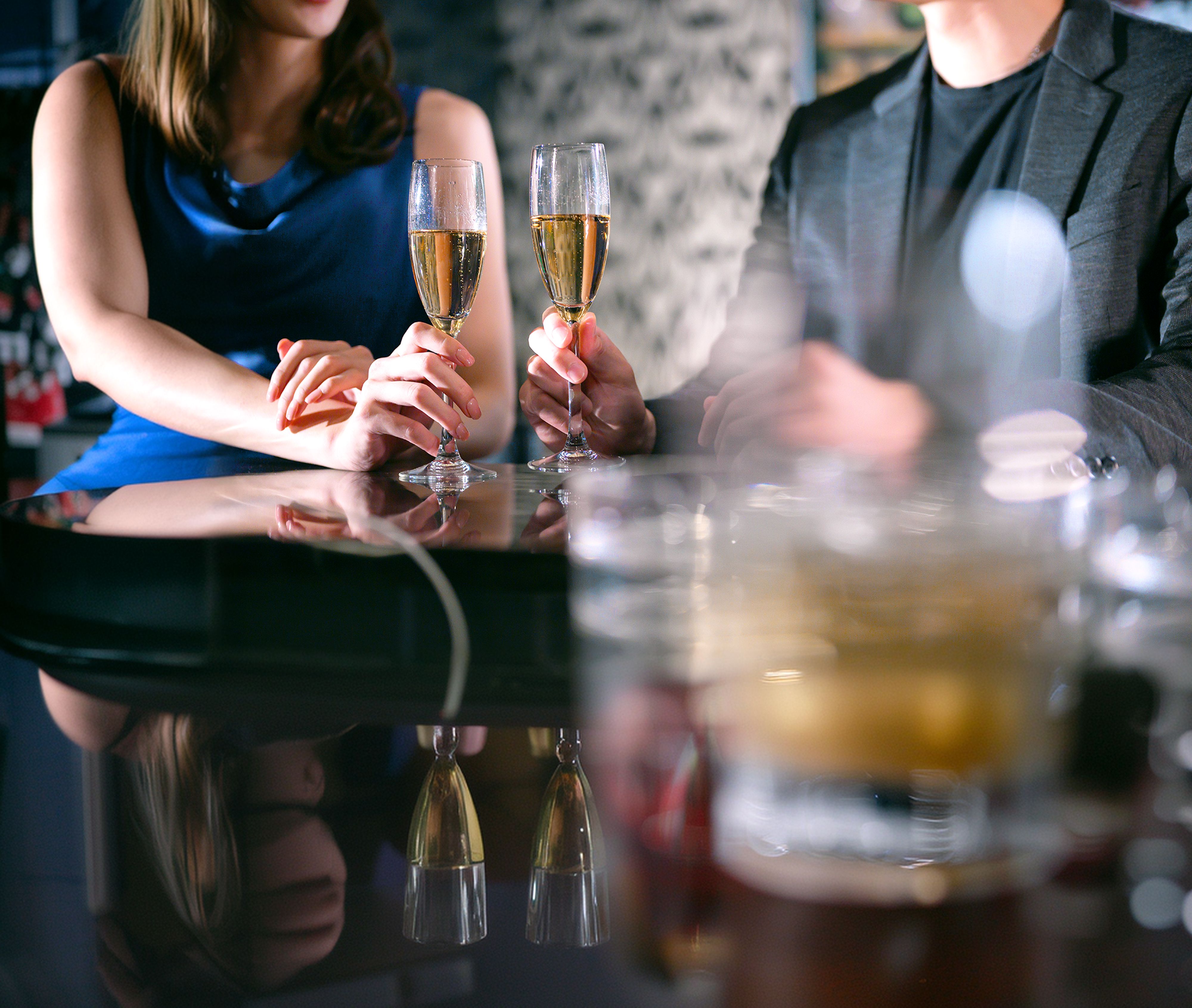 Two people holding champagne flutes at a reflective bar.