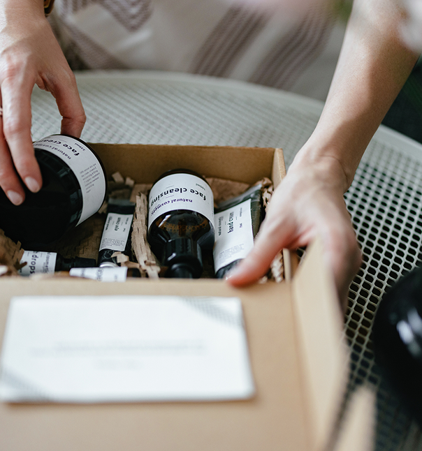 Person's hands placing or arranging skincare products in a cardboard box filled with shredded paper.