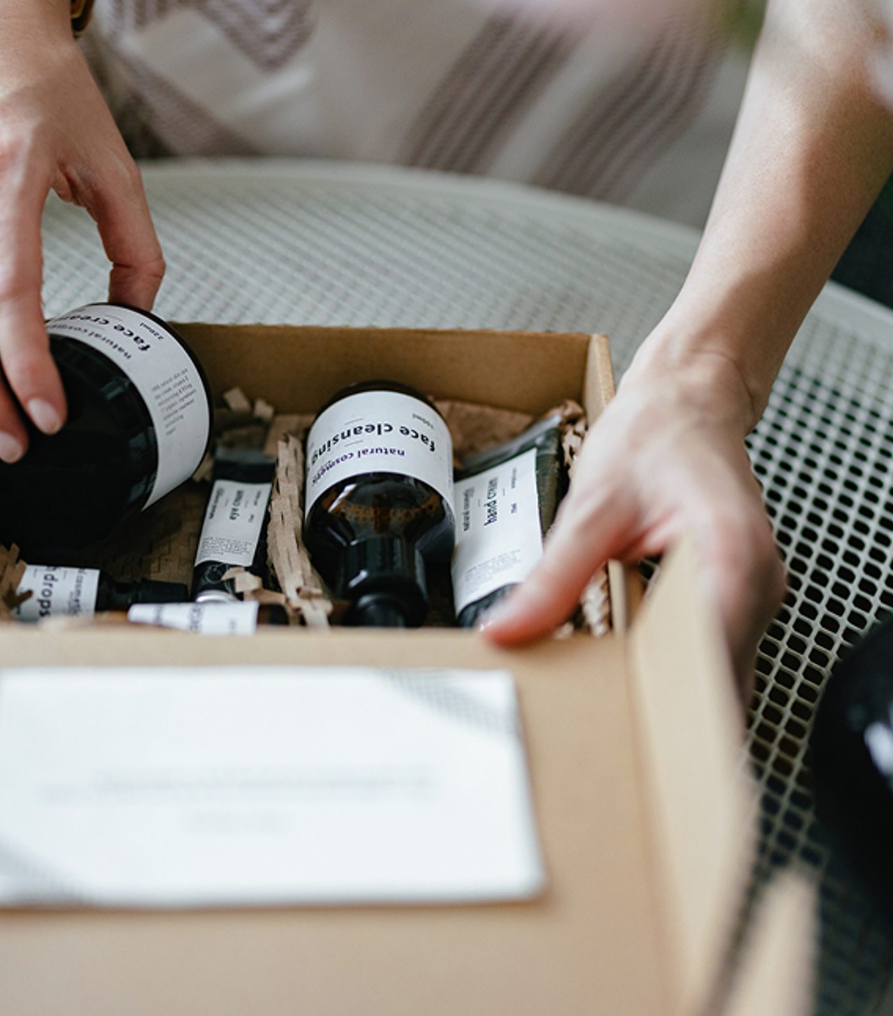 Person's hands placing or arranging skincare products in a cardboard box filled with shredded paper.