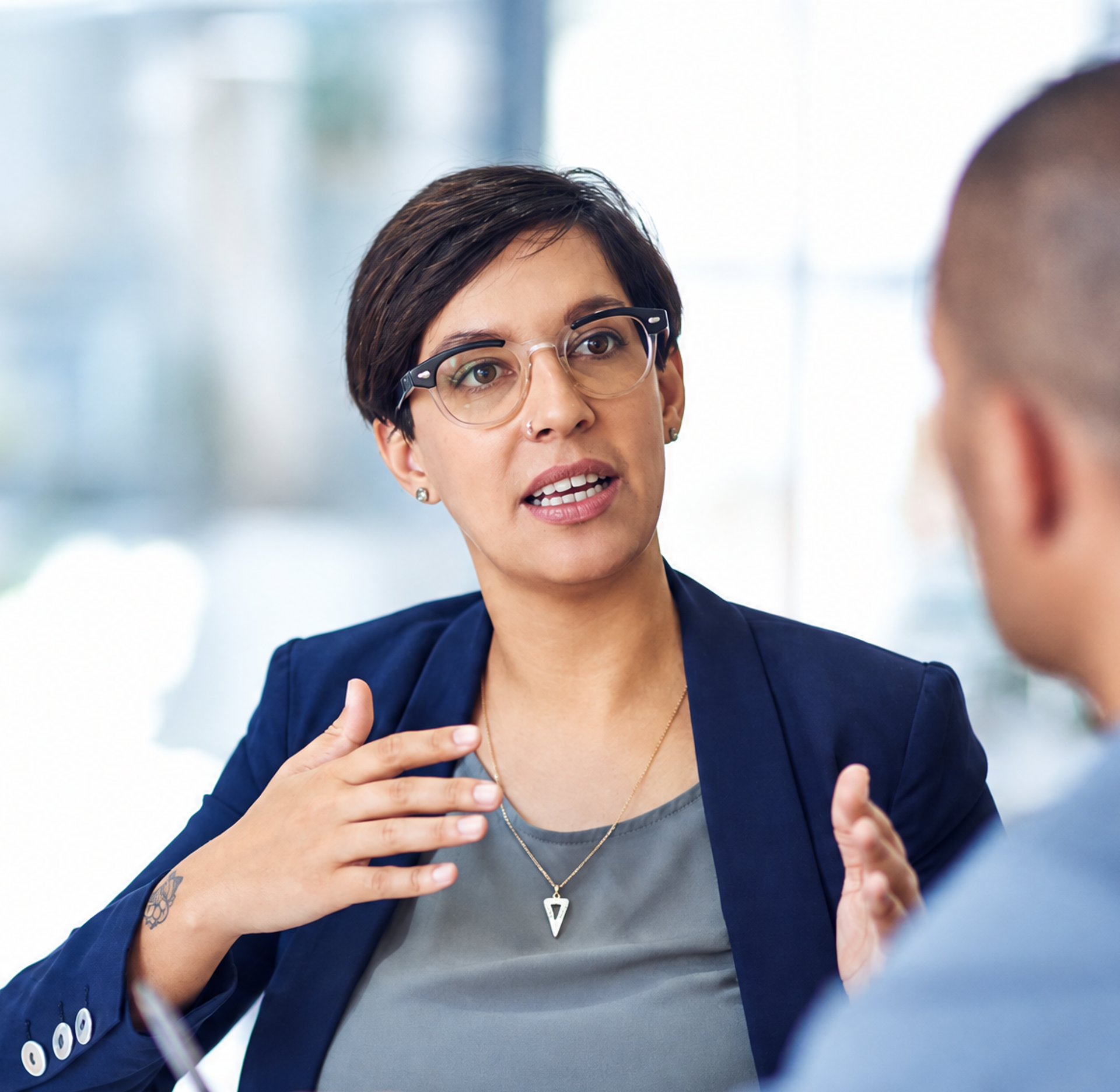 A woman with glasses actively speaks to two colleagues during a business meeting, with a laptop displaying a bar chart on the table.