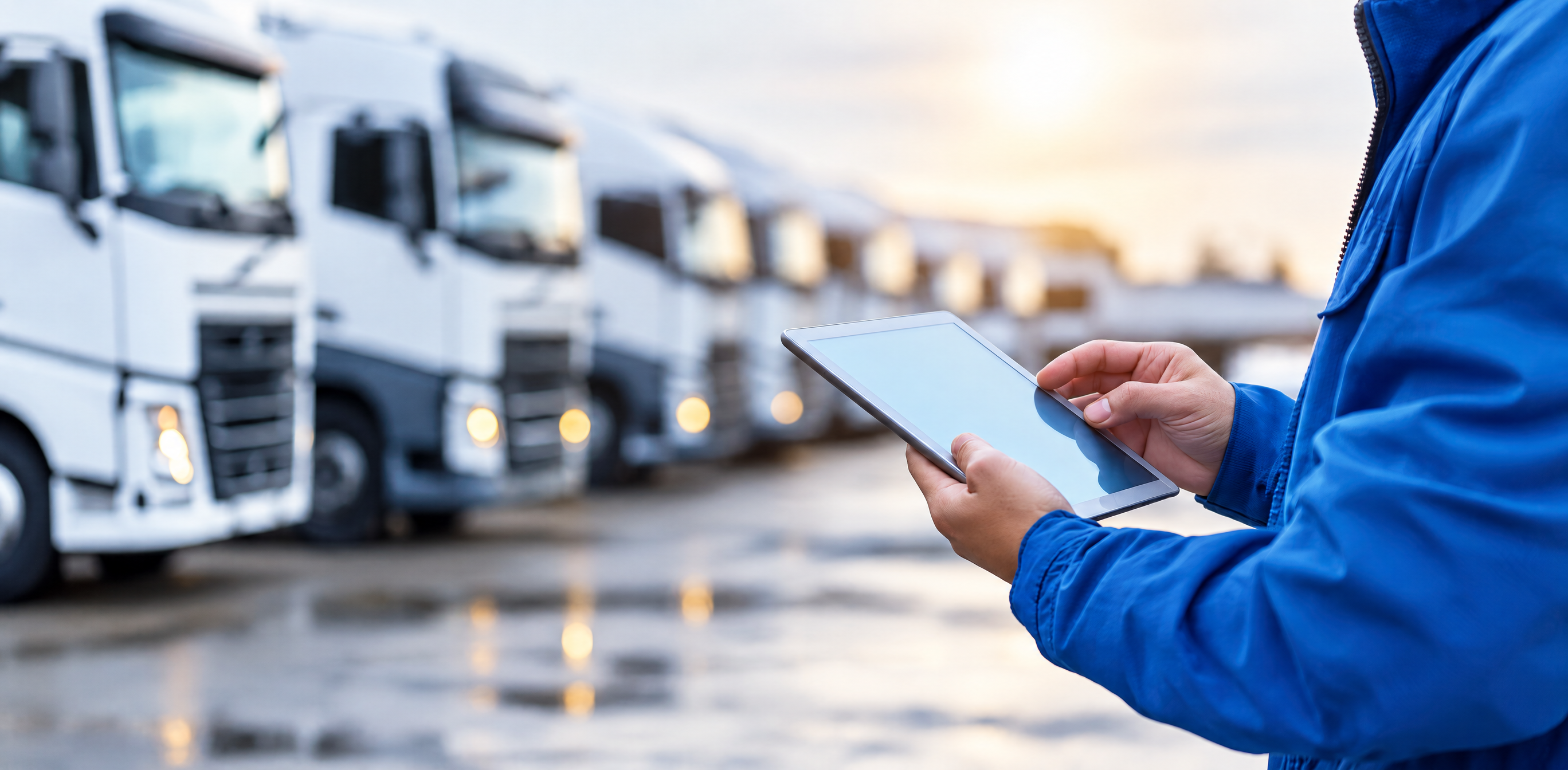 Person using a tablet with blurred white semi-trucks in the background.
