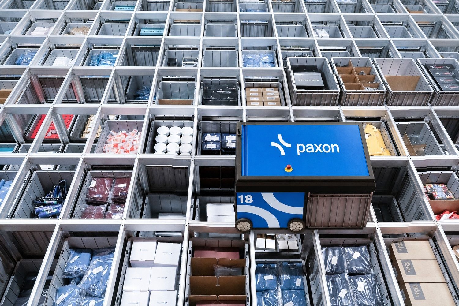 Un robot Paxon se déplace dans un système automatisé de stockage et de récupération sur grille, rempli de bacs de produits.