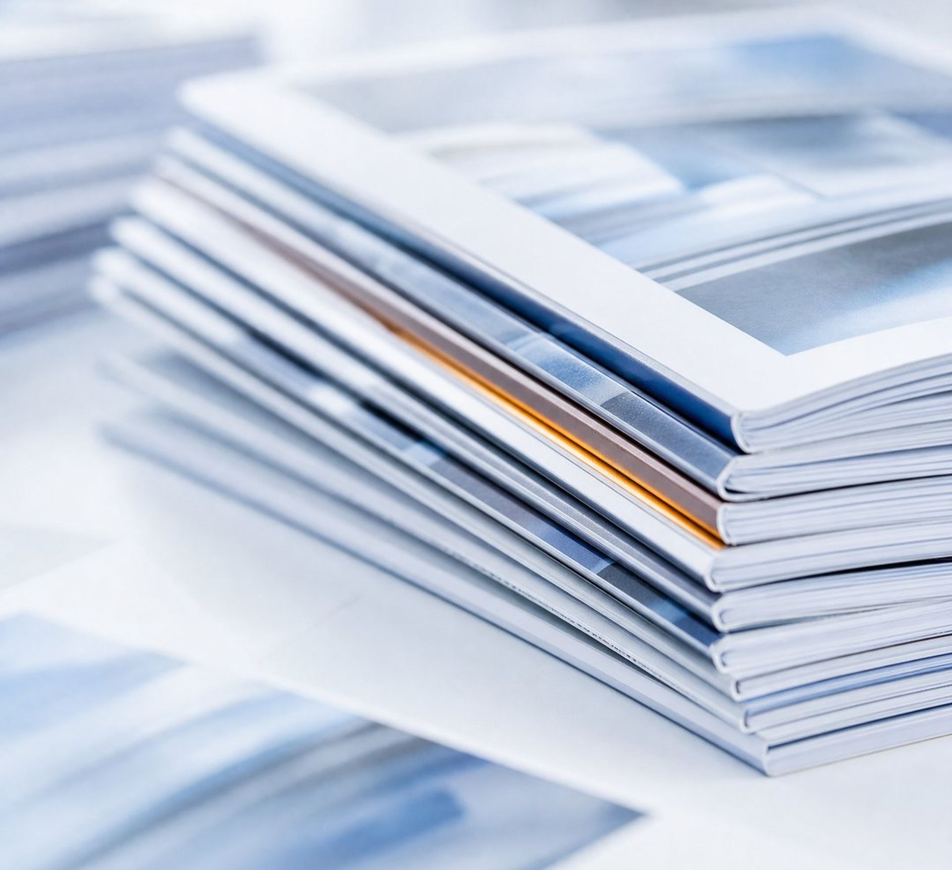 Stack of white-covered magazines with blue tones, one having an orange spine.