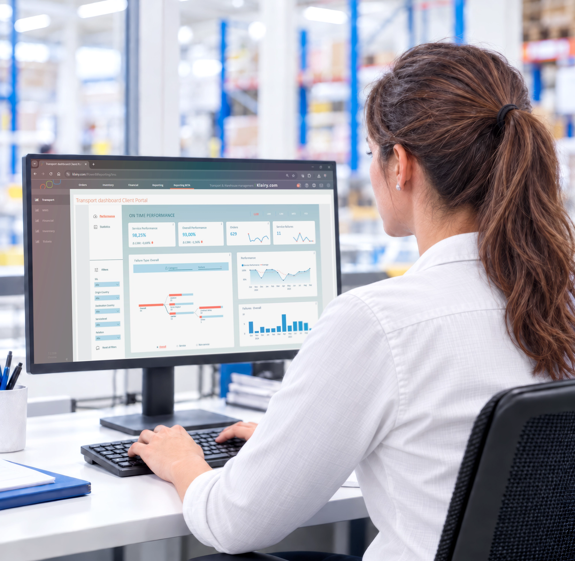 A woman views a "Transport dashboard Client Portal" with performance data on a computer screen in a warehouse.