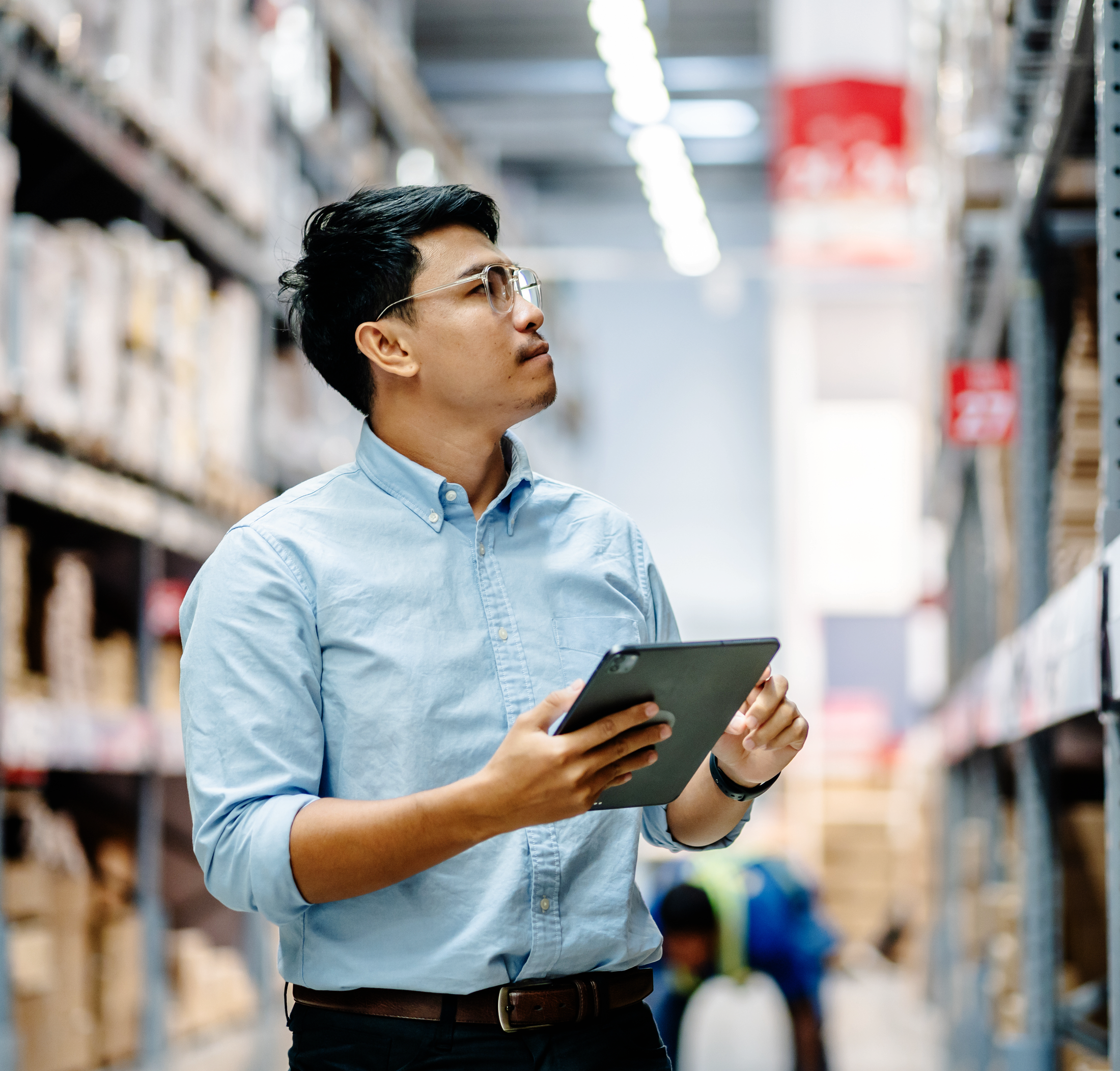 Man in a warehouse inspecting shelves with a tablet.