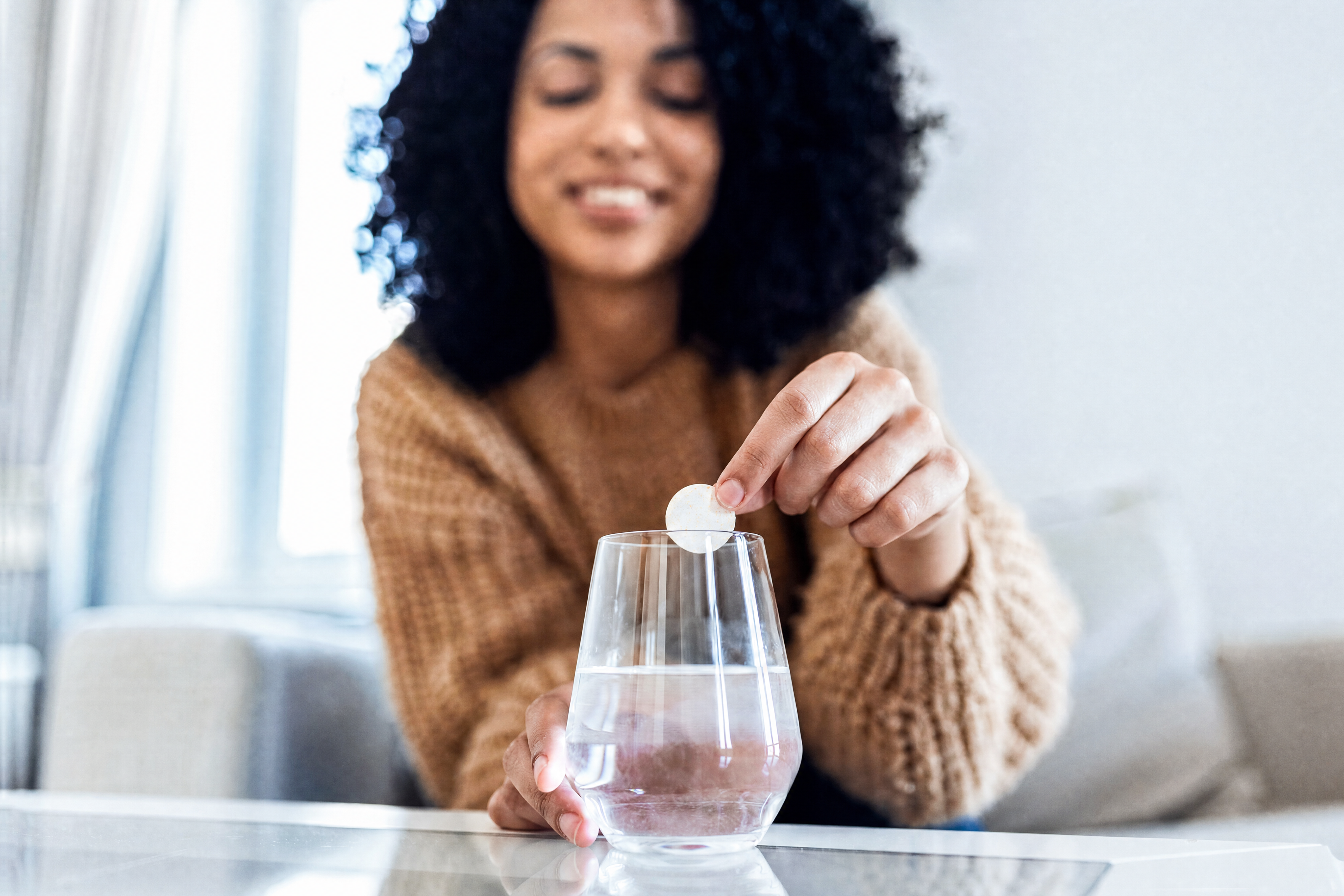 A smiling woman drops an effervescent tablet into a glass of water.