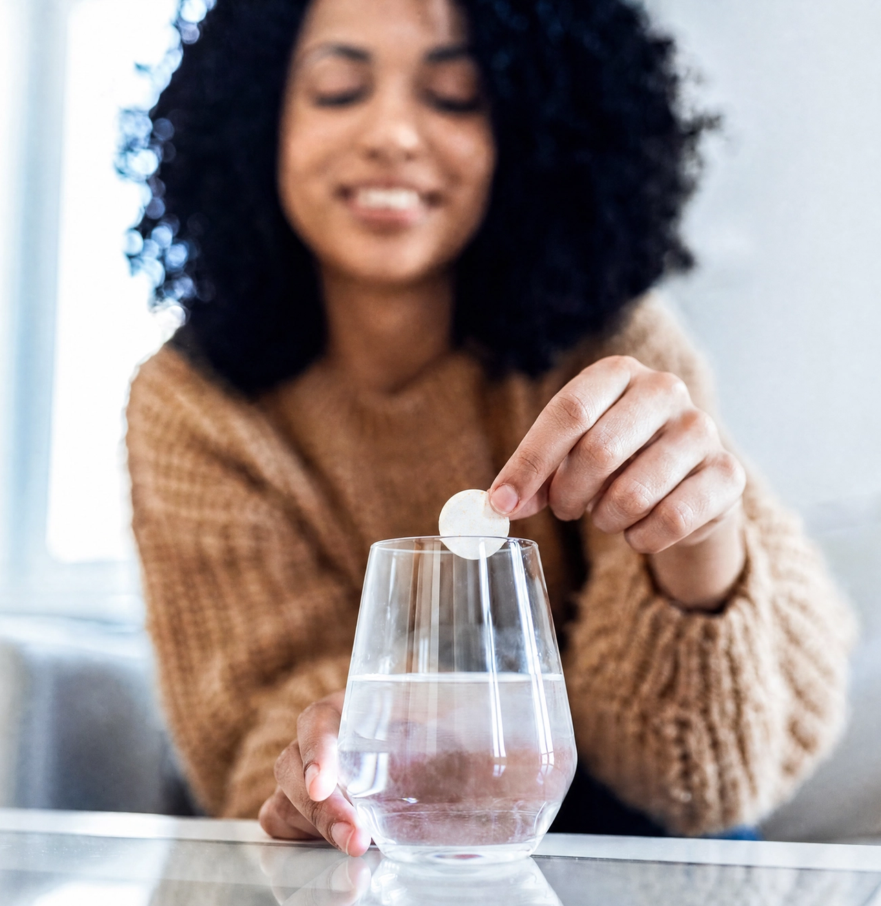 A smiling woman drops an effervescent tablet into a glass of water.