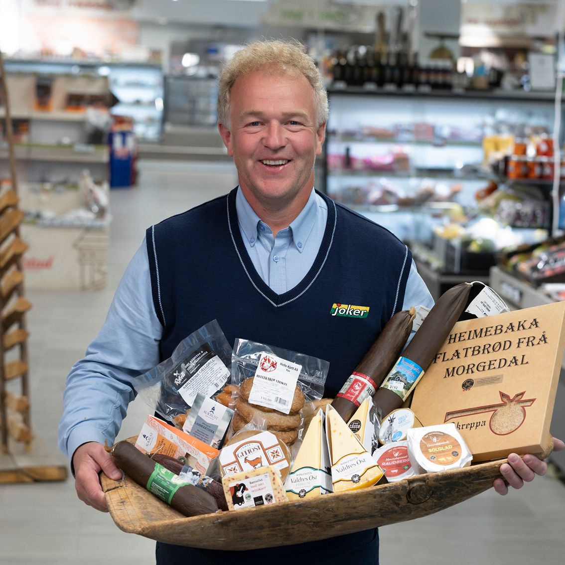 Kjøpmann Harald Lasskogen med lokalmat i et fat inne i butikken