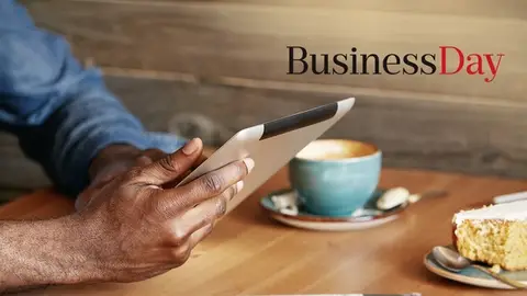 Man reading an article on his tablet with coffee and newspaper