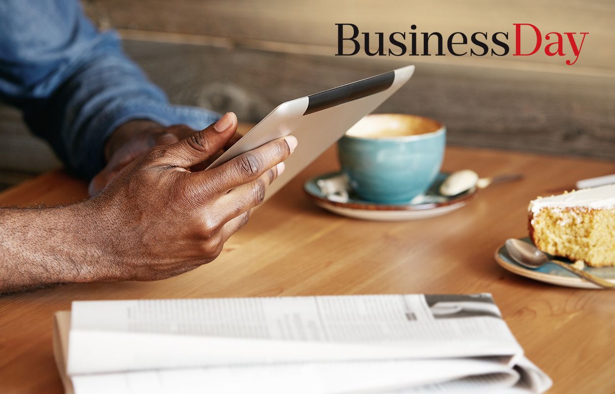 Man reading an article on his tablet with coffee and newspaper