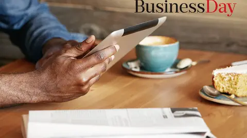 Man reading an article on his tablet with coffee and newspaper
