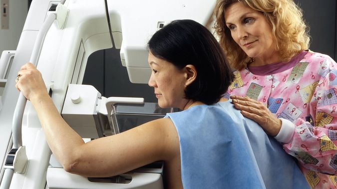 Woman Receives Mammogram. A Caucasian female technician positions an Asian woman at an imaging machine to receive a mammogram. Creator: Rhoda Baer