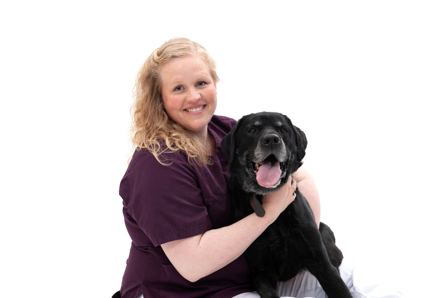 Kaja Røed, veterinær ved Tønsberg Dyreklinikk, sitter med armene rundt en svart hund mot hvit bakgrunn