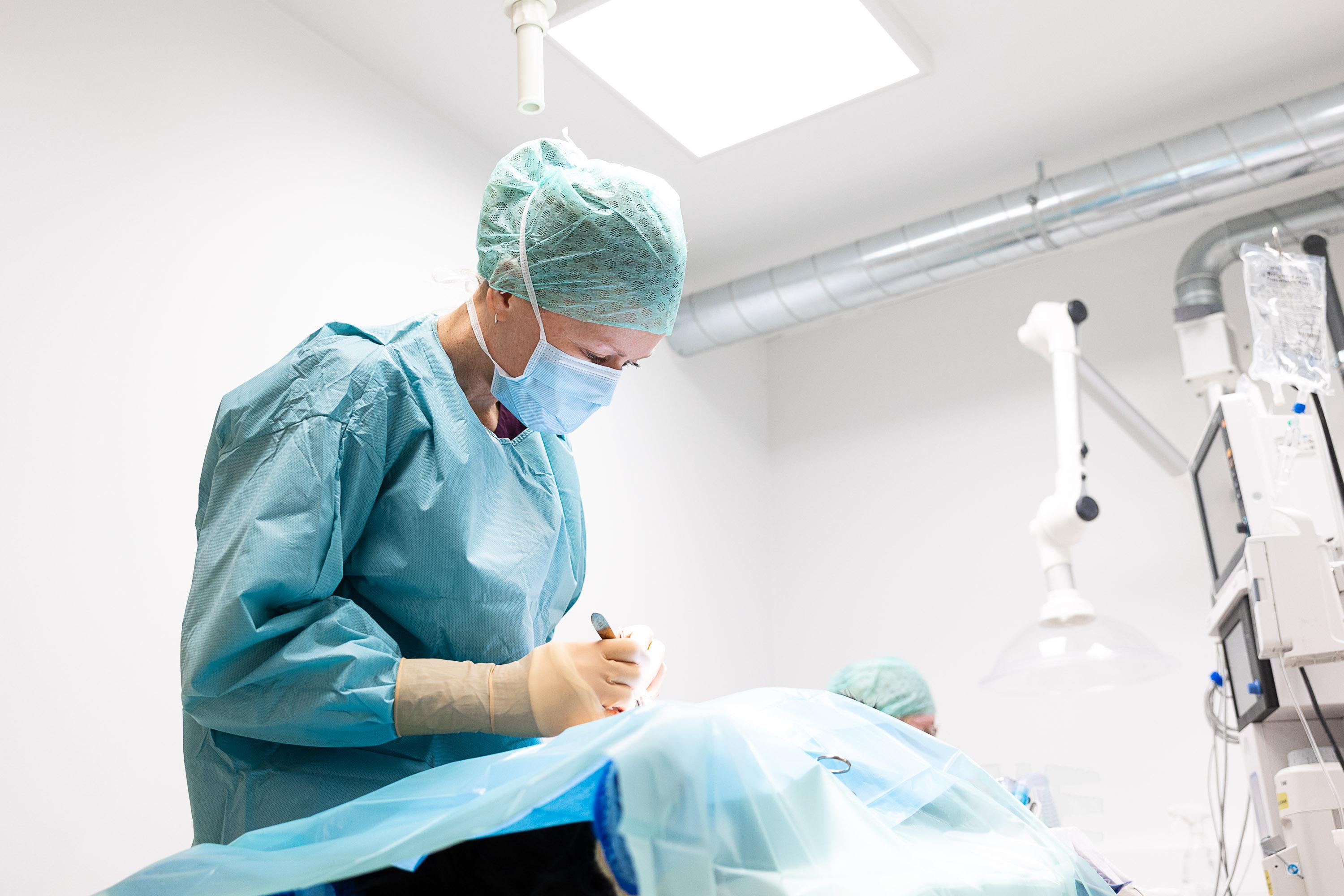 Ansatt i operasjonsfrakk og munnbind bøyd over det sterile operasjonsfeltet
