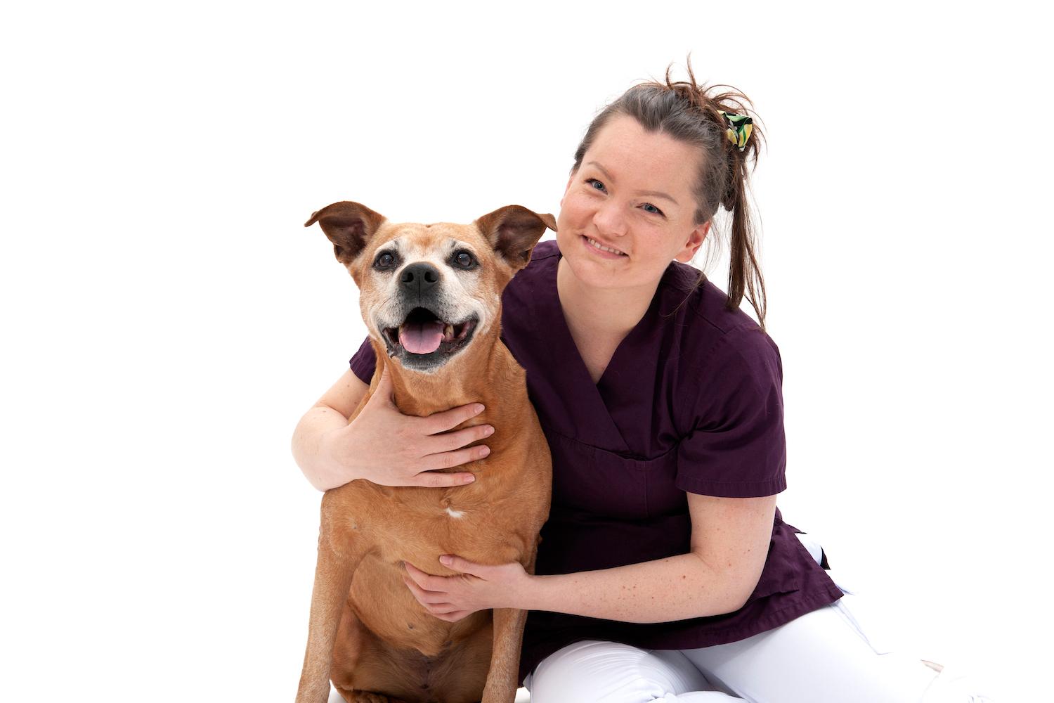 Sunniva Tilrem, veterinær ved Tønsberg Dyreklinikk, sitter med armene rundt en brun hund mot hvit bakgrunn