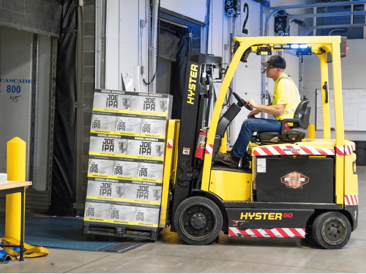 Electric forklift with a blue warning light on the overhead guard at a warehouse loading dock