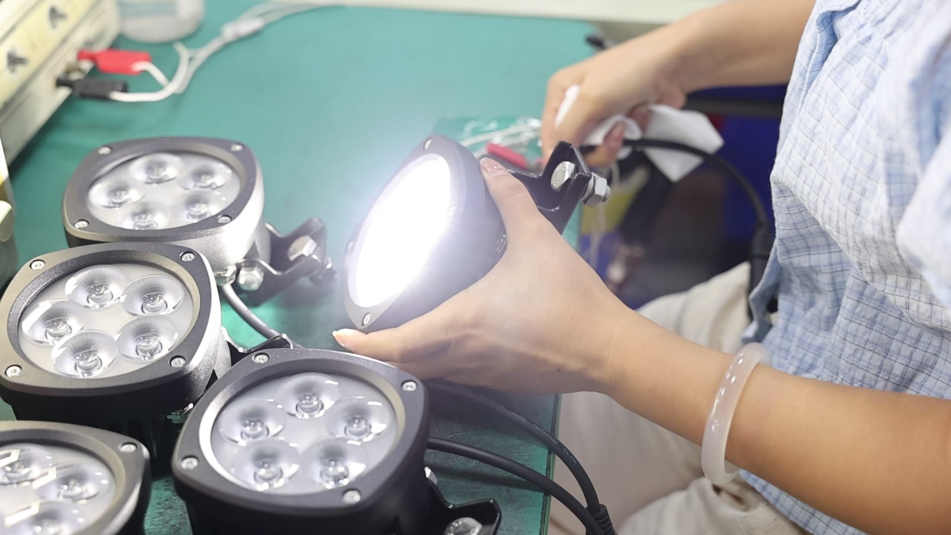 A technician evaluating a powered-on round LED work light on the test bench