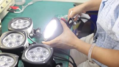 A technician evaluating a powered-on round LED work light on the test bench