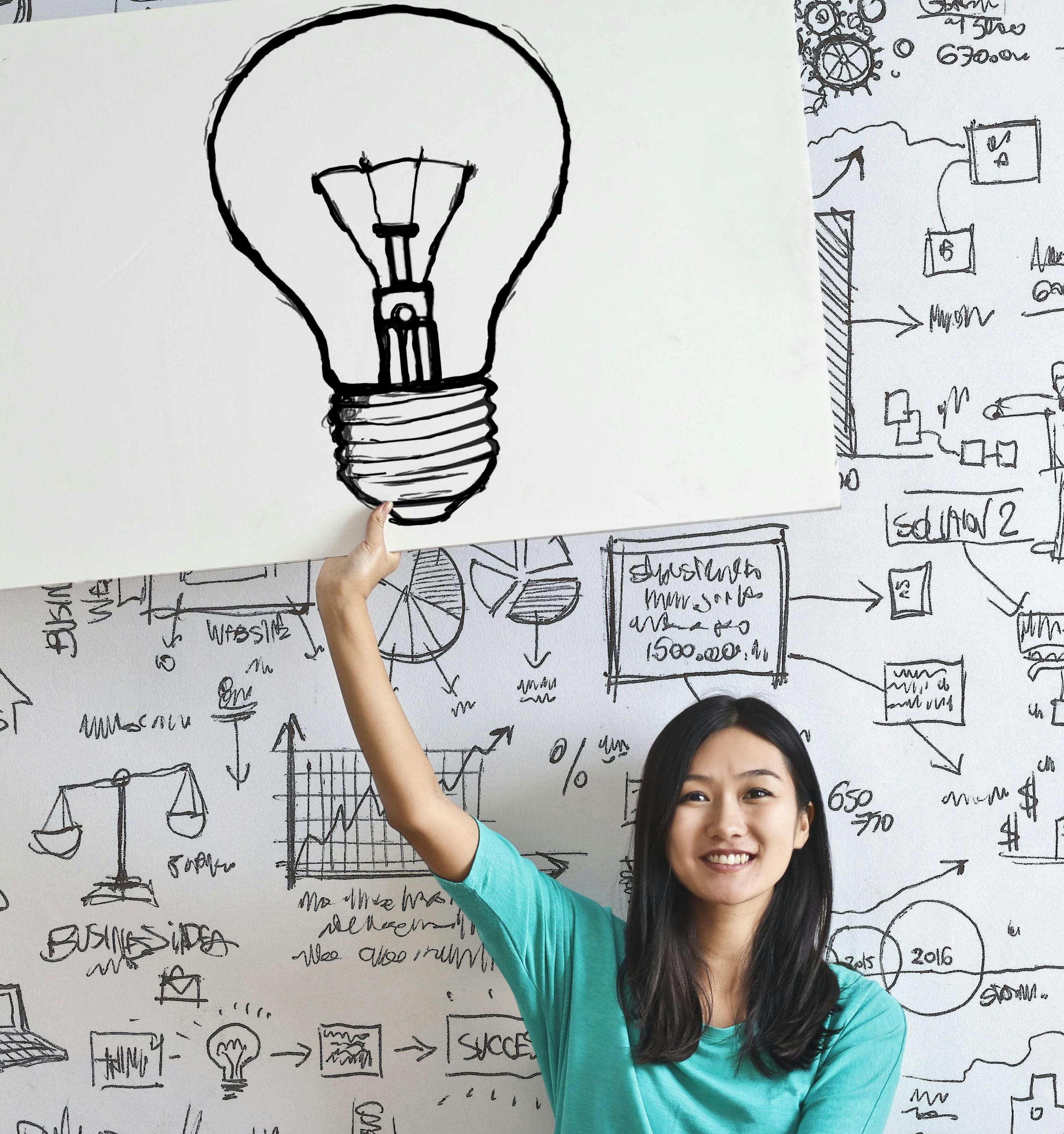 Woman smiling and holding up hand-drawn picture of a lightbulb