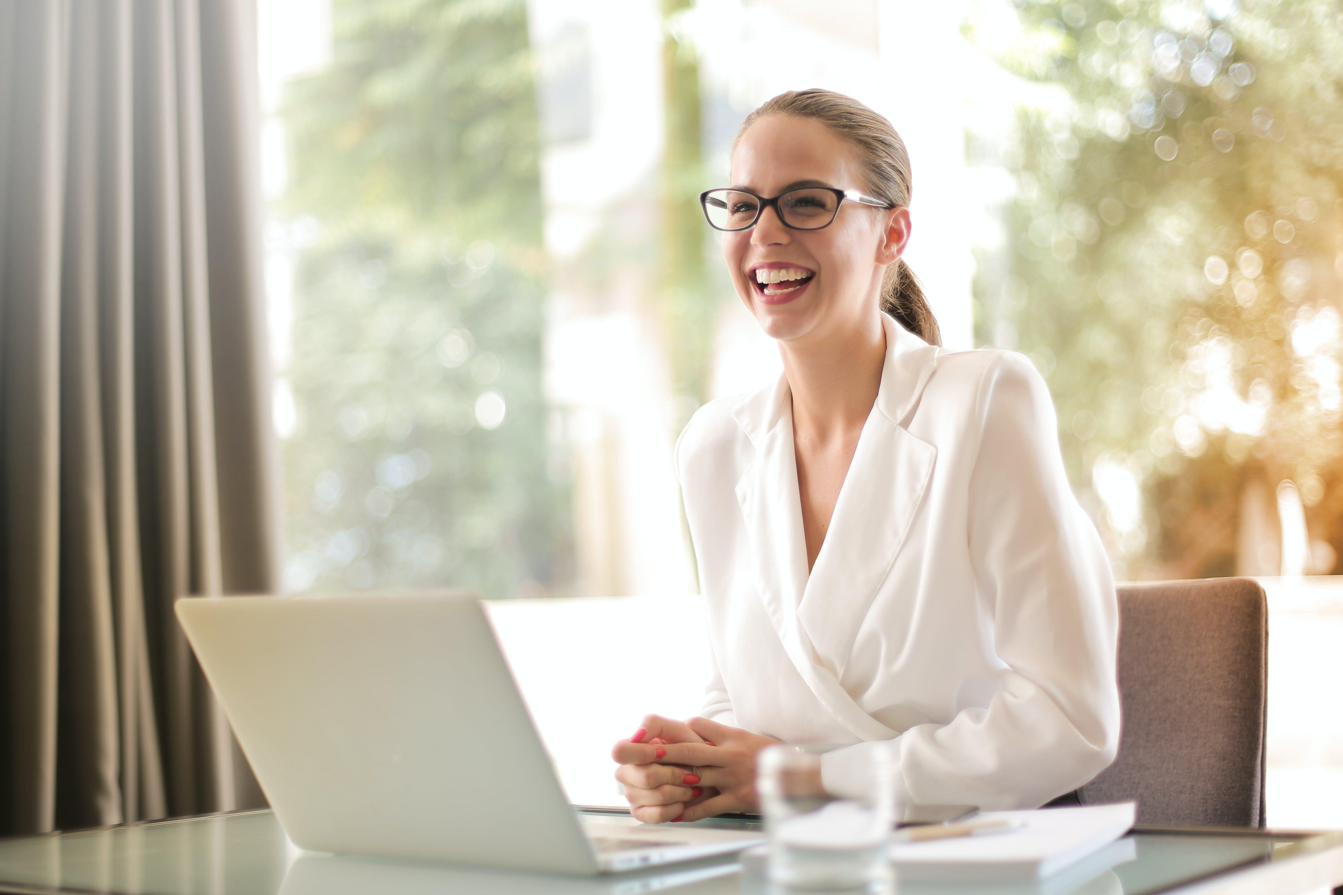 Business woman wearing glasses laughs while sitting at computer