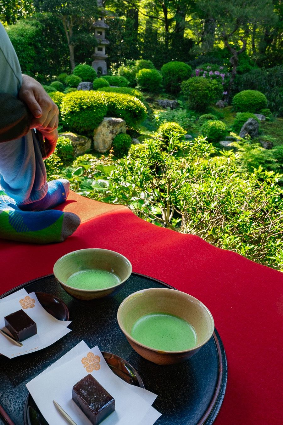 Deux bols de matcha et leurs wagashi posés sur un drap rouge, face au jardin du Sanzen-in