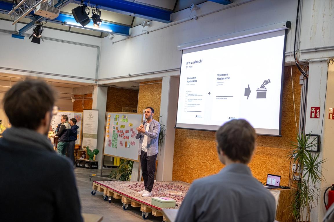 Moderator Feridun Öztoprak erklärt auf der Bühne das Matchingverfahren.