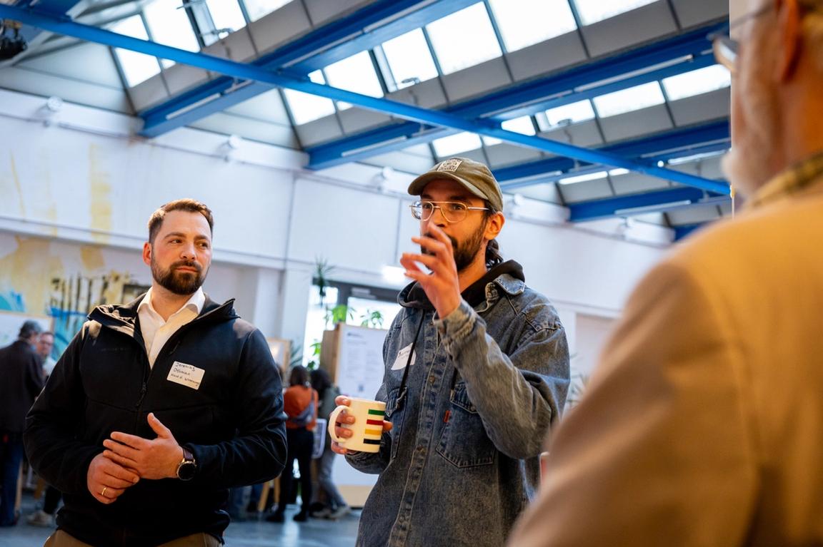 Teilnehmer mit Kaffeetasse in der Hand diskutiert seinen Lösungsvorschlag mit anderen Teilnehmenden.