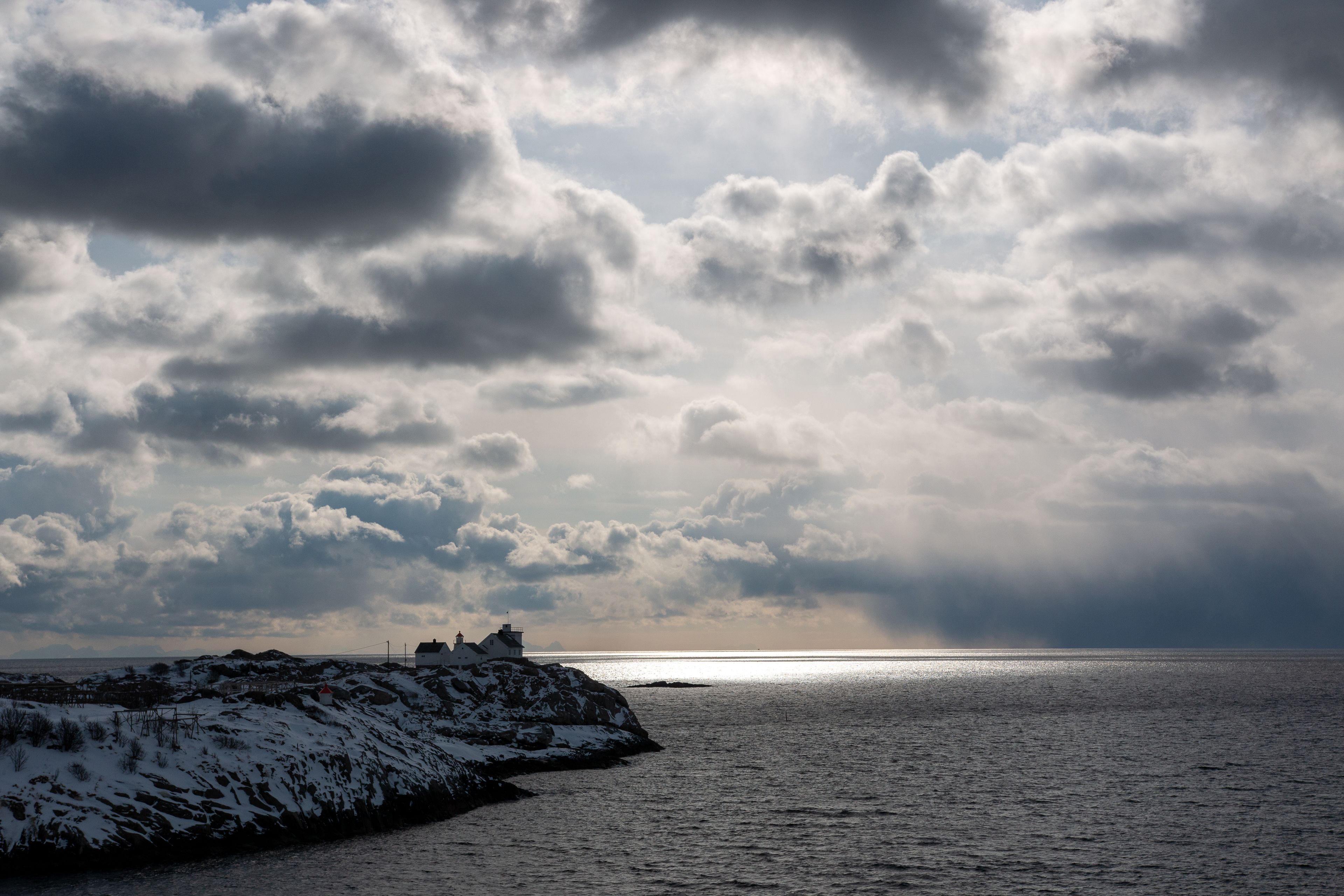 The lighthouse in Henningsvær, Stormy weather in the background with shimmers of sunshine