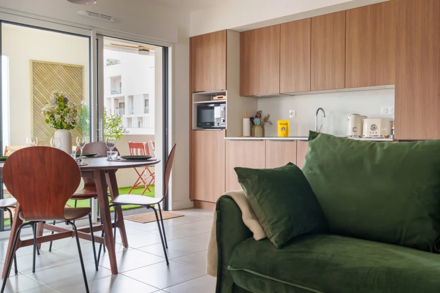 Vue d'ensemble du séjour de L'Esplanade : cuisine, coin repas et canapé vert