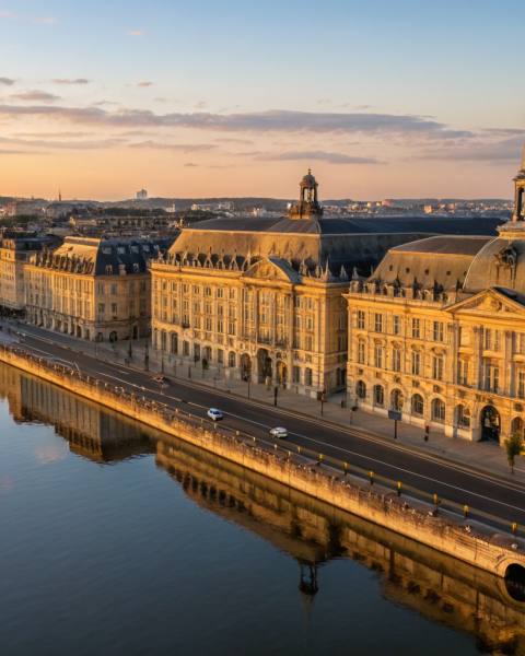 Vue aérienne des quais bordelais et du miroir d'eau à heure dorée, façade calcaire 18e siècle de la Place de la Bourse reflétée dans l'eau